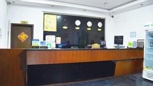 A reception desk with a wooden counter, a computer monitor, a small refrigerator, and a wall clock. - Mingxing Hotel (Shanghai)