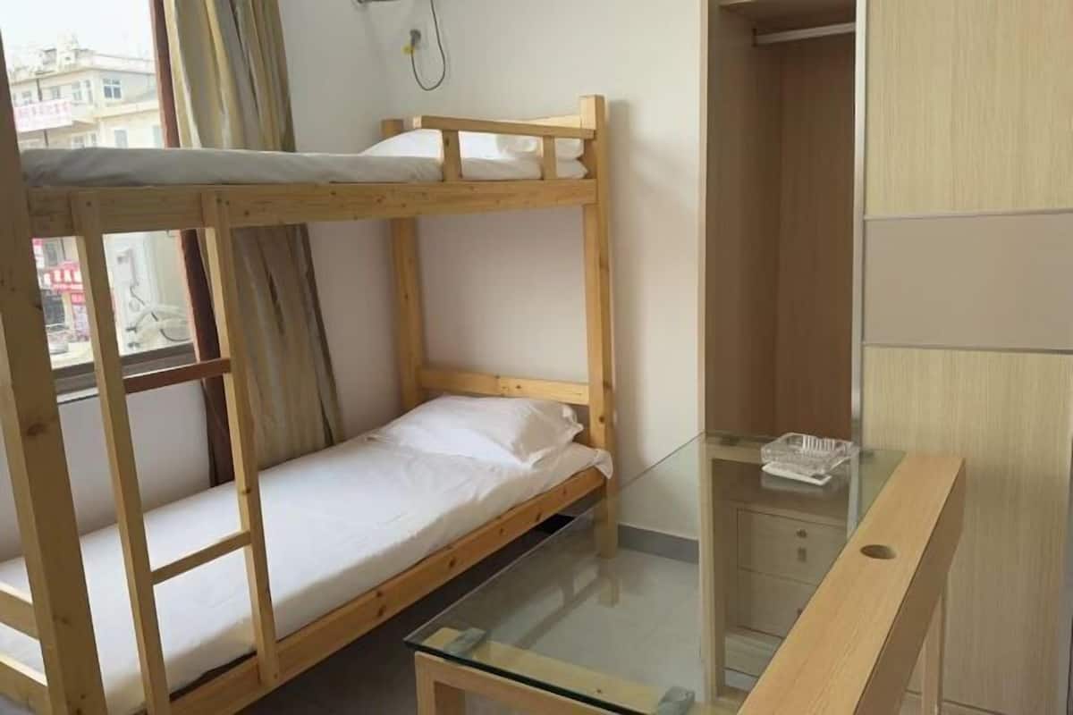 Une chambre avec un lit superposé, une table en verre et une armoire.