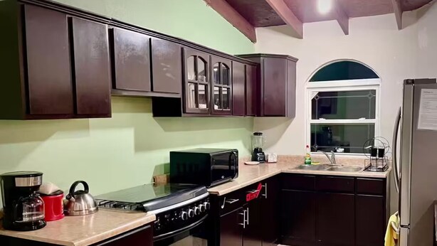 A kitchen with dark wooden cabinets, a gas stove, a microwave, and a sink. - San Quintín Casa Skov (San Quintín)