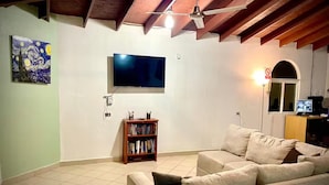 A living room with a beige sofa, a bookshelf, a flat-screen TV, and a ceiling fan. - San Quintín Casa Skov (San Quintín)