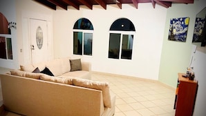 A living room with a beige sofa, two arched windows, and a wooden cabinet. - San Quintín Casa Skov (San Quintín)