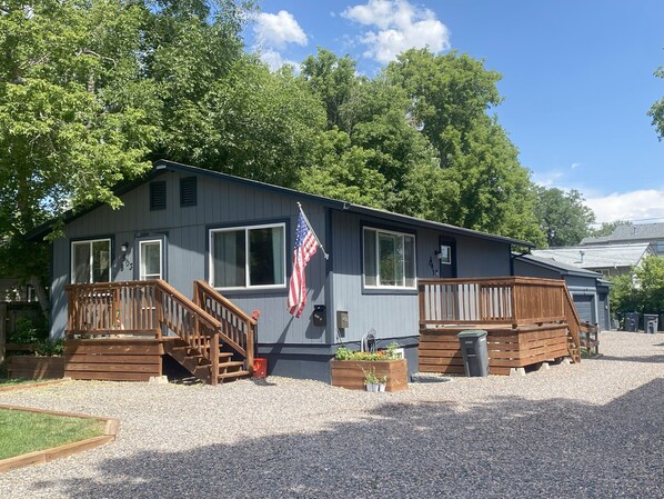 A single-story cabin with a front porch, a flag, and a small garden area.