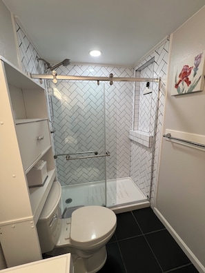 A bathroom with a toilet, a shower enclosure, and a tiled floor.