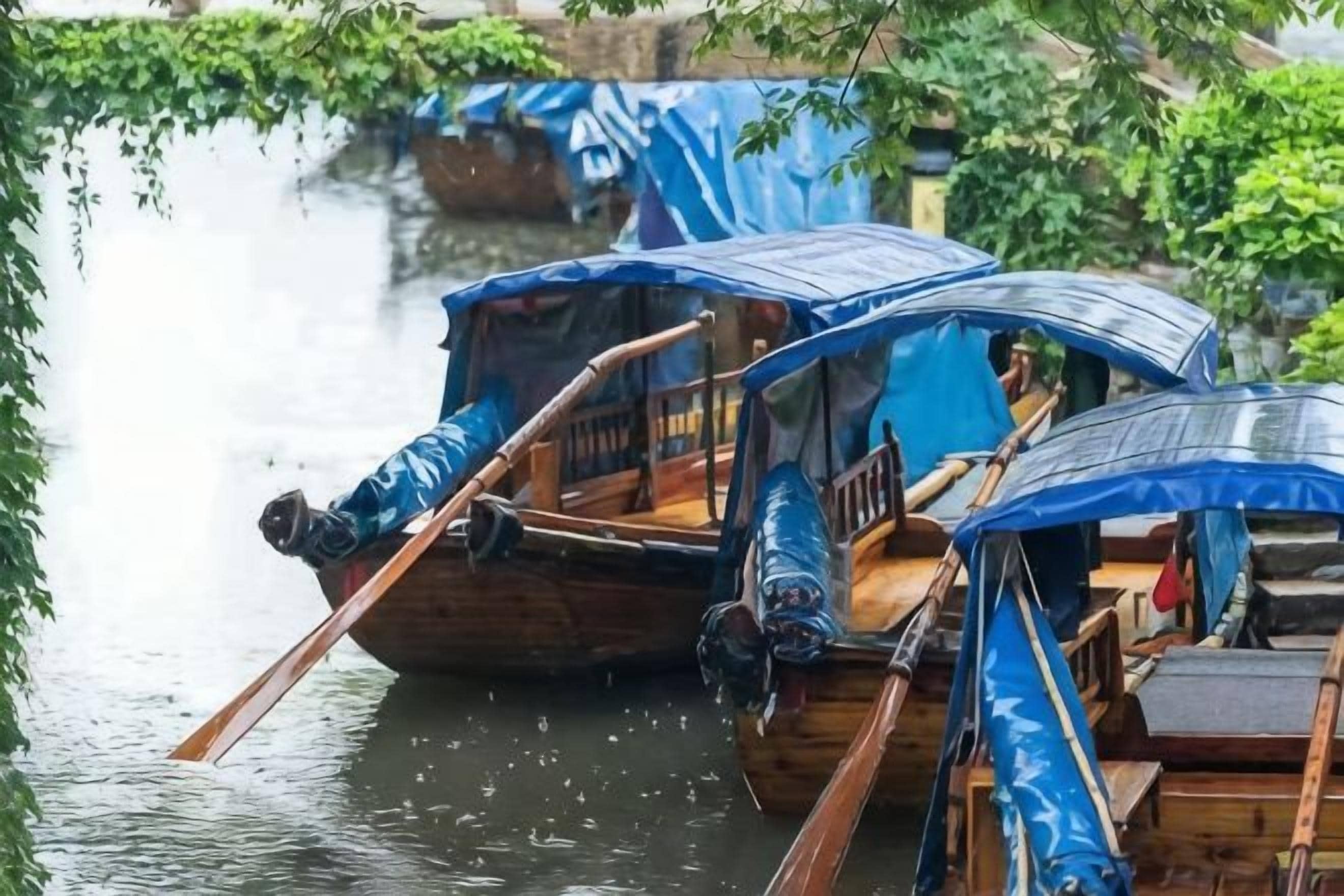 Deux bateaux traditionnels en bois, surmontés de toiles bleues, sont amarrés dans une étendue d’eau calme.