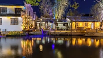 A traditional building with a water body in front, featuring a wooden structure with lights and a staircase leading to the entrance.
