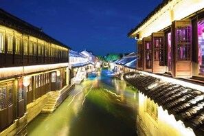 A narrow waterway flanked by traditional buildings with illuminated facades and wooden walkways. - Duyun Yuxiang Inn (Kunshan)