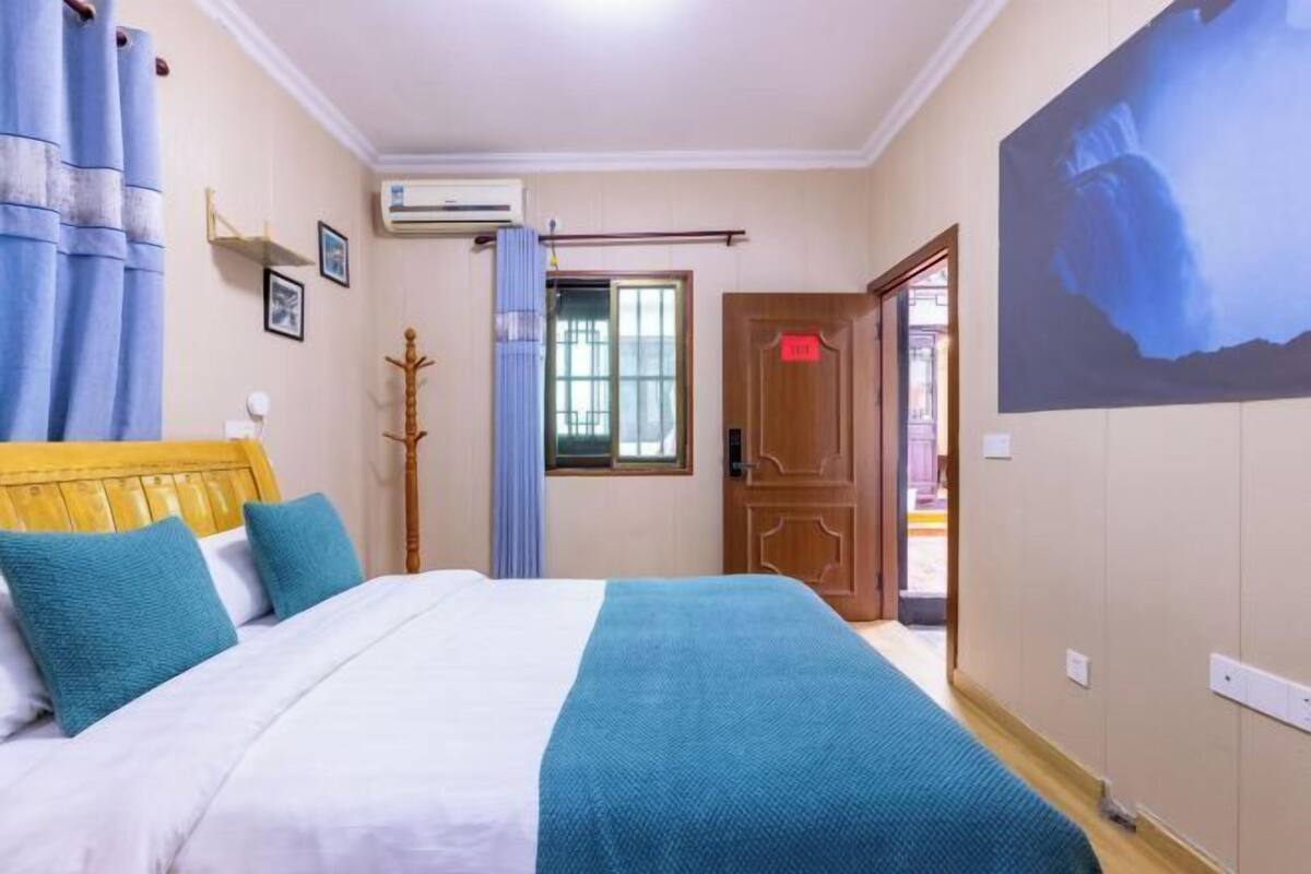 Una camera da letto con un letto, tende, un condizionatore d'aria a parete, una porta e un quadro.