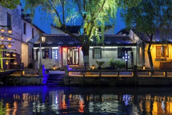A traditional Chinese courtyard with a water feature, wooden bridges, and illuminated buildings. - Duyun Yuxiang Inn (Kunshan)