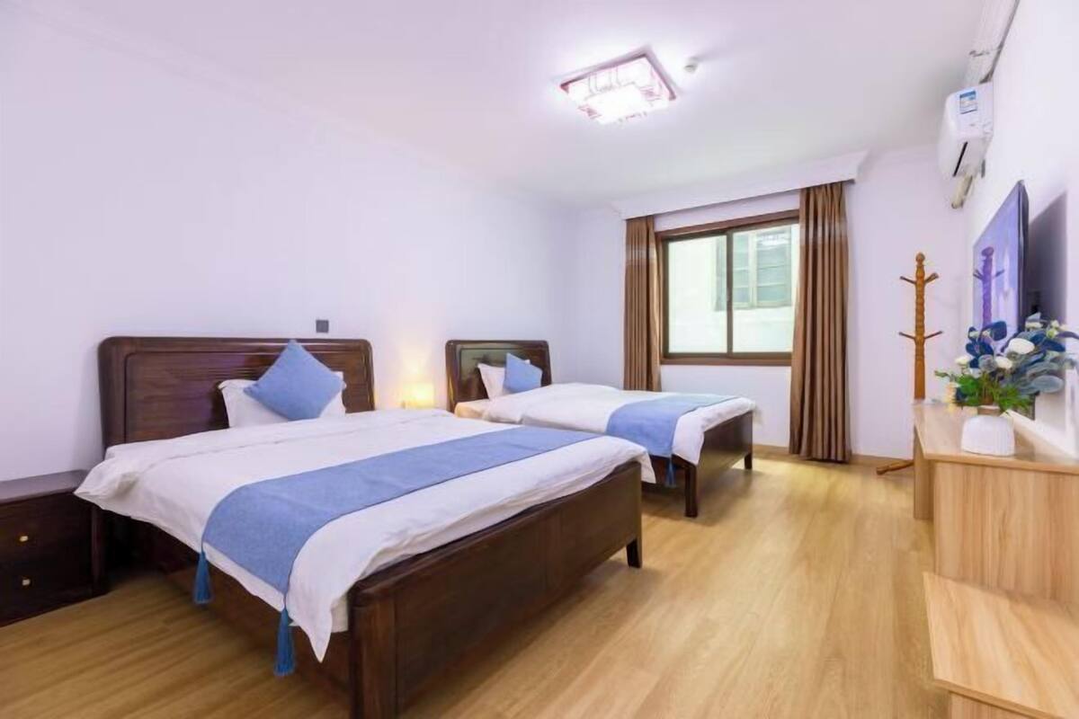 Camera d'albergo con due letti, una cassettiera in legno, una finestra con tende e una lampada a soffitto.