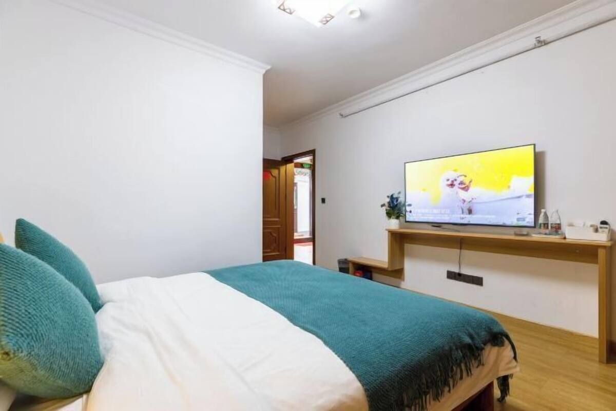 Una camera da letto con un letto, una televisione su uno scaffale in legno e una porta che dà su un'altra stanza.
