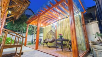 An outdoor patio area with a wooden pergola, seating, and a hanging chair.