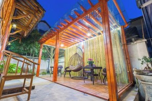 An outdoor patio area with a wooden pergola, seating, and a hanging chair. - Duyun Yuxiang Inn (Kunshan)