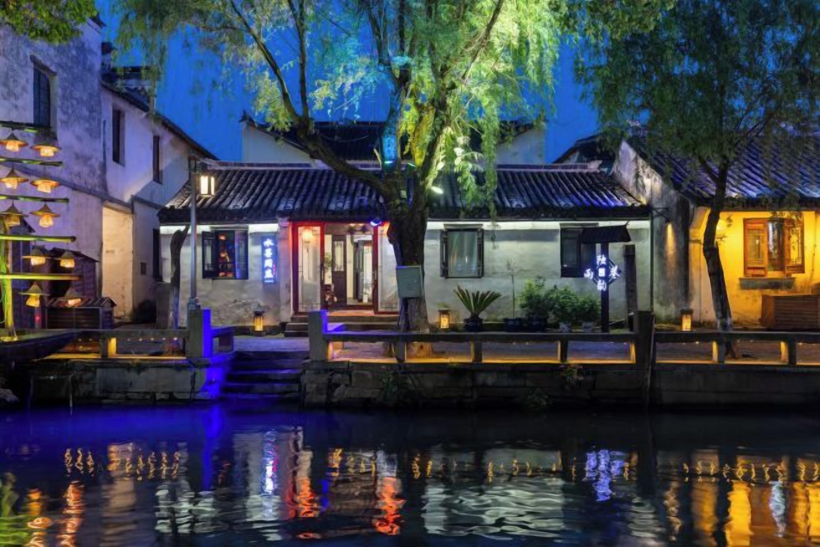 A traditional Chinese courtyard with buildings, a waterway, and illuminated structures.