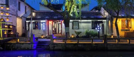 A traditional Chinese courtyard with buildings, a waterway, and illuminated structures.