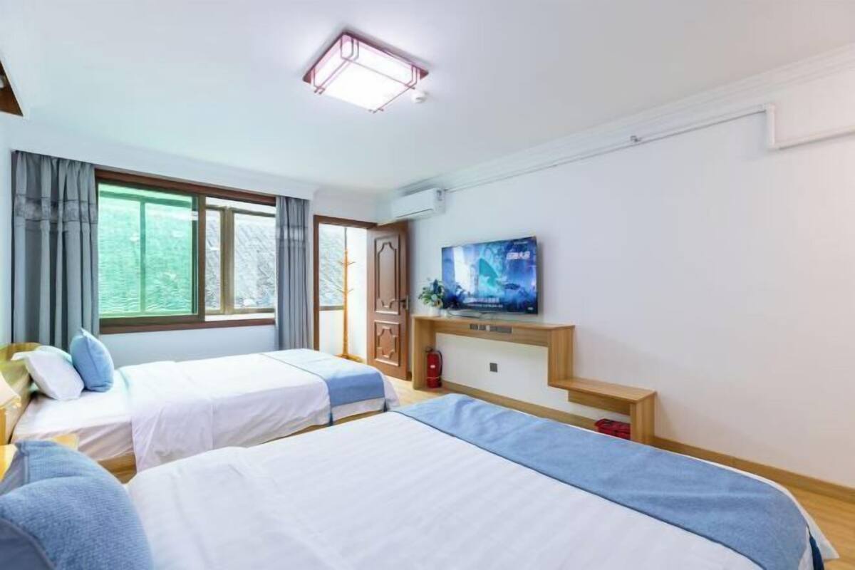 Una camera d'albergo con due letti, una televisione a parete e una finestra con tende.