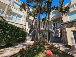 A multi-story building with outdoor staircases, a garden with flowers, and a clear blue sky.