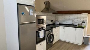 A compact kitchen with a refrigerator, oven, microwave, and washing machine. - Loli's Attic (Luarca)
