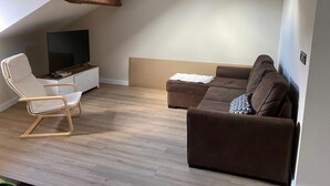 A modern living room with a flat-screen TV, a white chair, and a brown sofa. - Loli's Attic (Luarca)