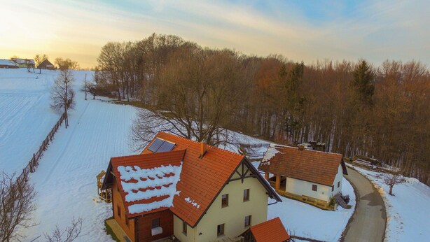 A rural house with a sloped roof, a small attached structure, and a snow-covered yard.
