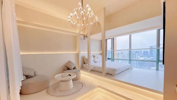Quarto de hotel moderno com uma janela grande, um candelabro, um sofá e uma pequena mesa.