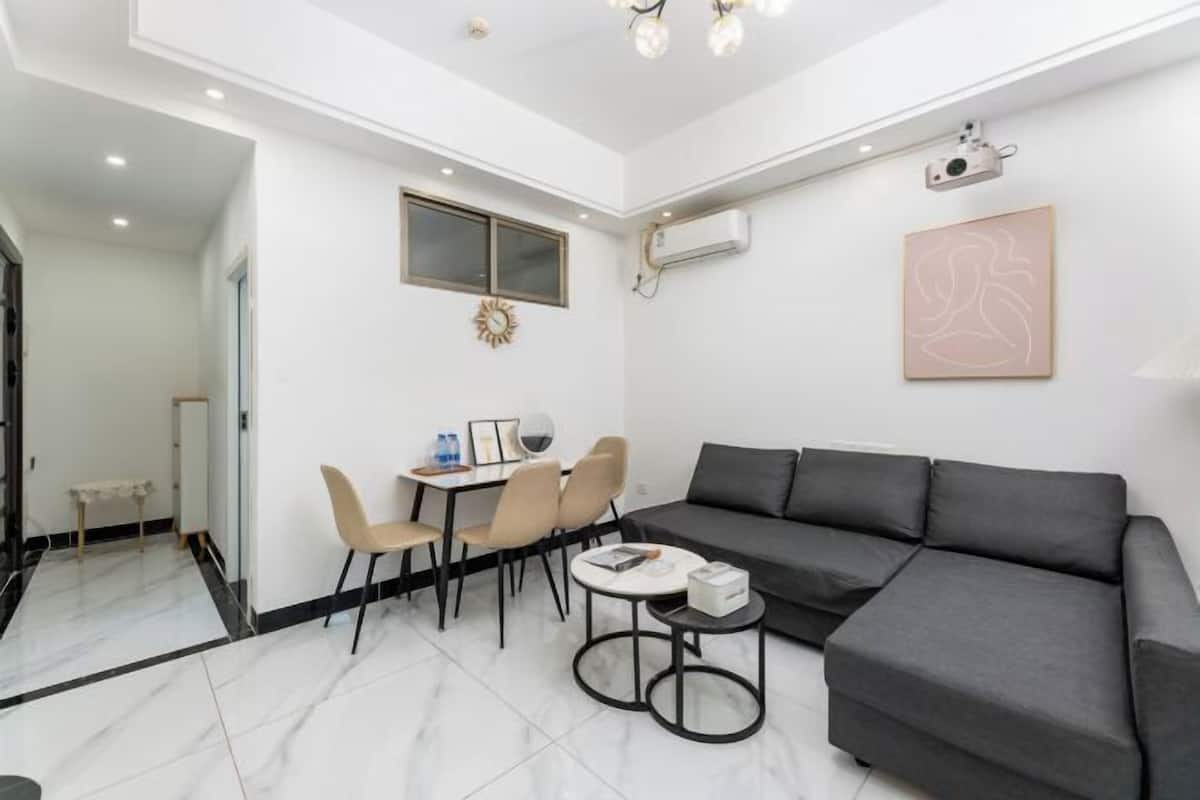 A modern living room with a grey sofa, a small round table, and a dining area with chairs and a table.