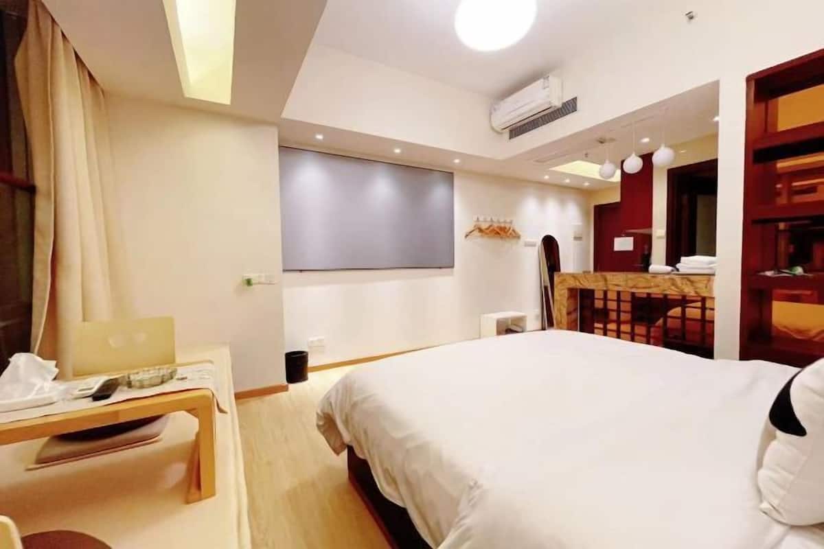 A hotel room with a bed, a desk with a laptop, a TV on the wall, and a small table with a chair.
