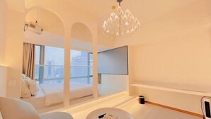 Quarto de hotel moderno com uma janela grande, televisão de tela plana, lustre e área de estar com uma mesa pequena.