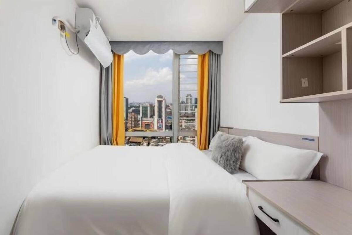 A hotel room with a bed, a desk, a view of the city, and a window with curtains.