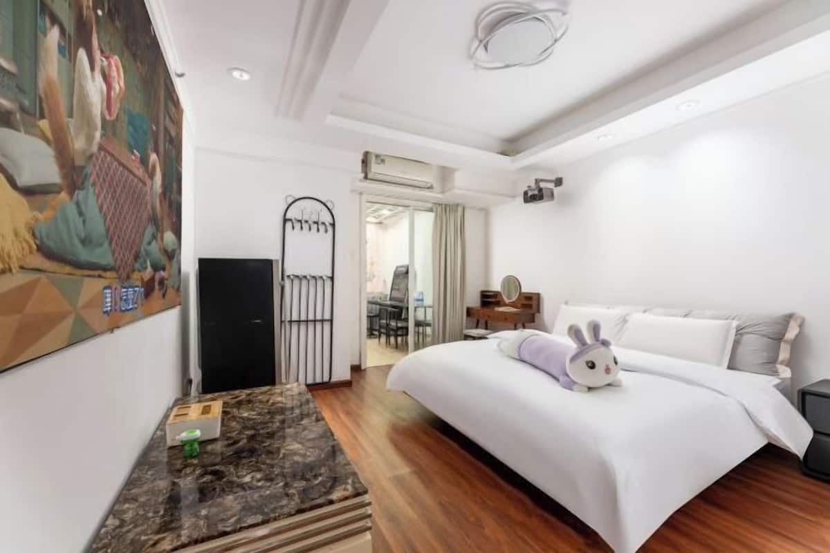 A hotel room with a bed, a small table, a chair, a mirror, and a painting on the wall.