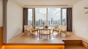 Quarto de hotel moderno com uma grande janela, uma mesa redonda, duas cadeiras e um tapete pequeno.