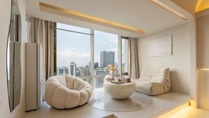 Uma sala de estar moderna com um sofá, uma mesa de centro redonda e vista para o horizonte urbano através de grandes janelas.