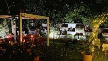 Un'area patio all'aperto con tavoli e sedie, circondata da piante in vaso e un pergolato in legno.