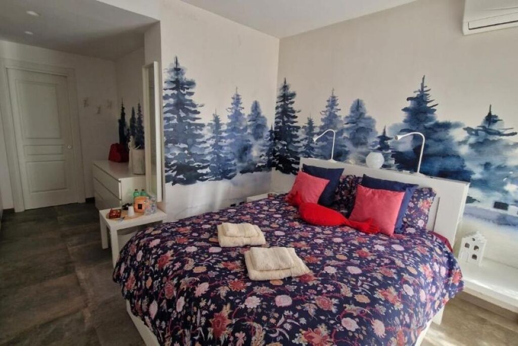Una camera da letto con un letto, un comodino e un affresco raffigurante alberi.