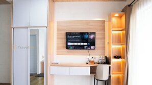Una habitación de hotel moderna con un escritorio de madera, un televisor de pantalla plana montado en la pared, una silla blanca y un armario empotrado.