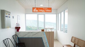 Un área de recepción con mostrador, dos sillas de madera, un banco y vistas a la montaña a través de amplios ventanales.