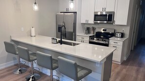 Una cocina moderna con una isla central, taburetes de bar, electrodomésticos de acero inoxidable e iluminación colgante.