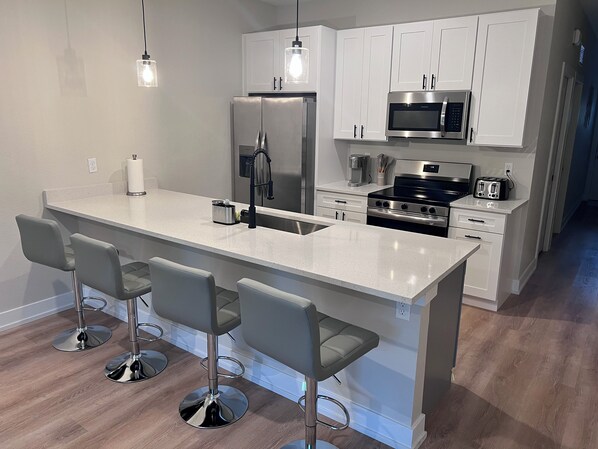 Una cocina moderna con una isla central, taburetes de bar, electrodomésticos de acero inoxidable e iluminación colgante.