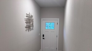 Un pasillo con una puerta blanca, un ventanal pequeño y una obra de arte abstracto colgada en la pared.