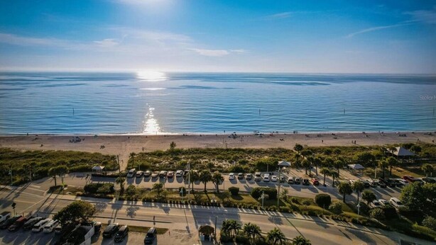 Vista aérea de una zona costera con playa, aparcamiento y cielo azul despejado.