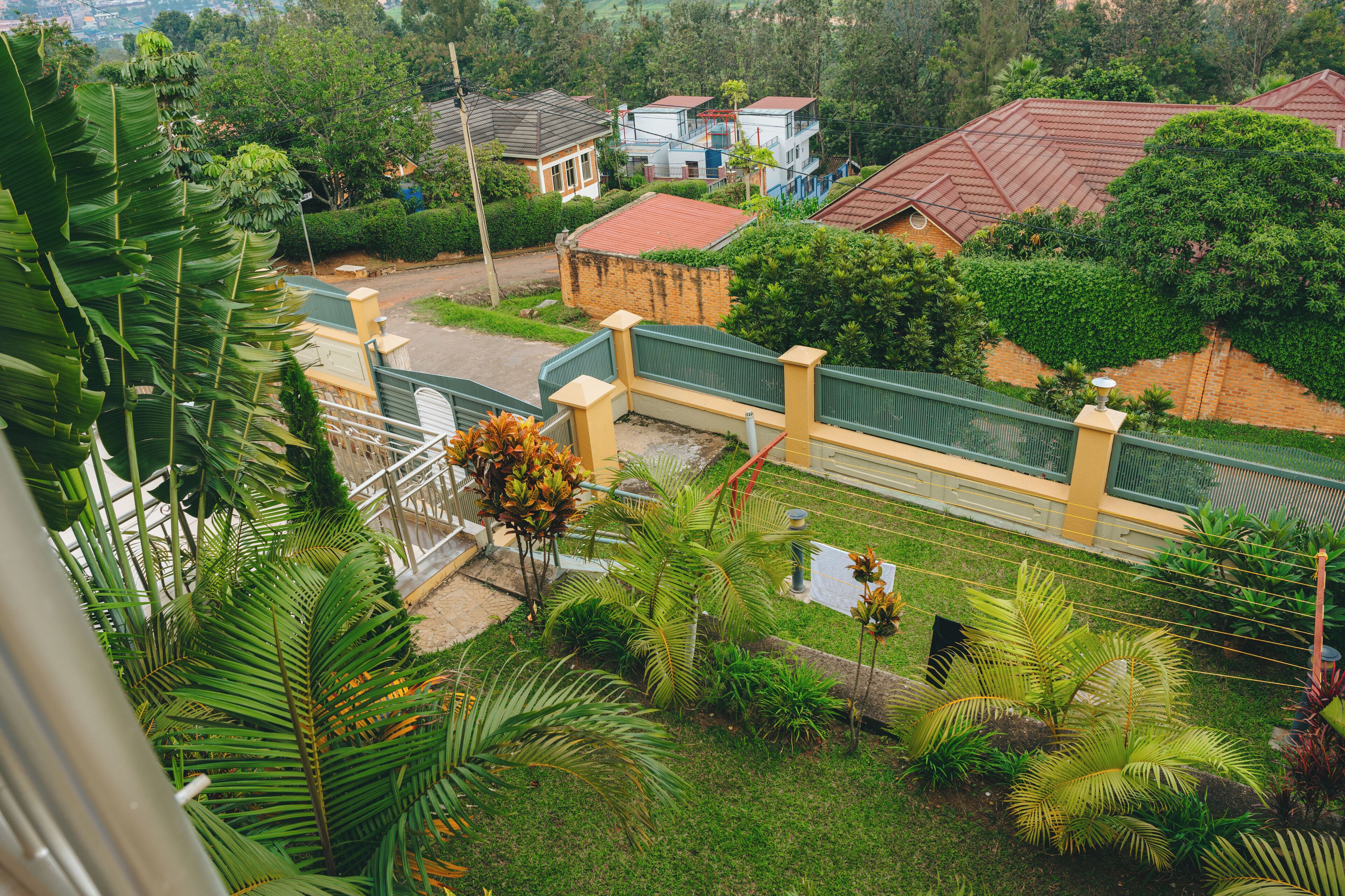 A residential area with houses, a green fence, and lush vegetation.