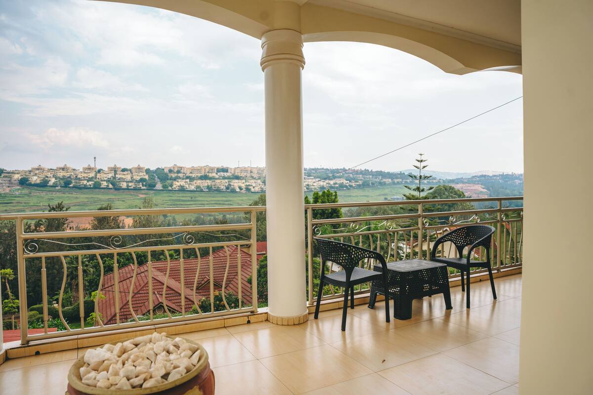 A balcony with a view of a town, two chairs, and a table.