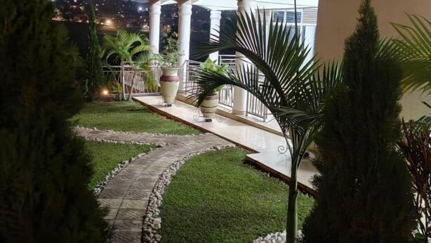 A multi-story building with a covered outdoor area, featuring a pathway, potted plants, and a view of a distant cityscape at night. - Mamba Residence (Kigali)