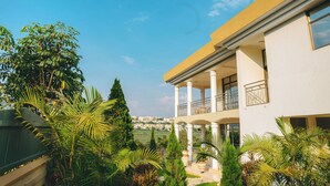 A modern two-story building with a balcony, surrounded by lush greenery and a clear view of the cityscape in the background. - Mamba Residence (Kigali)