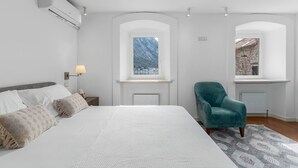 Une chambre avec un grand lit, deux fenêtres donnant sur un beau paysage, un fauteuil turquoise et un radiateur.