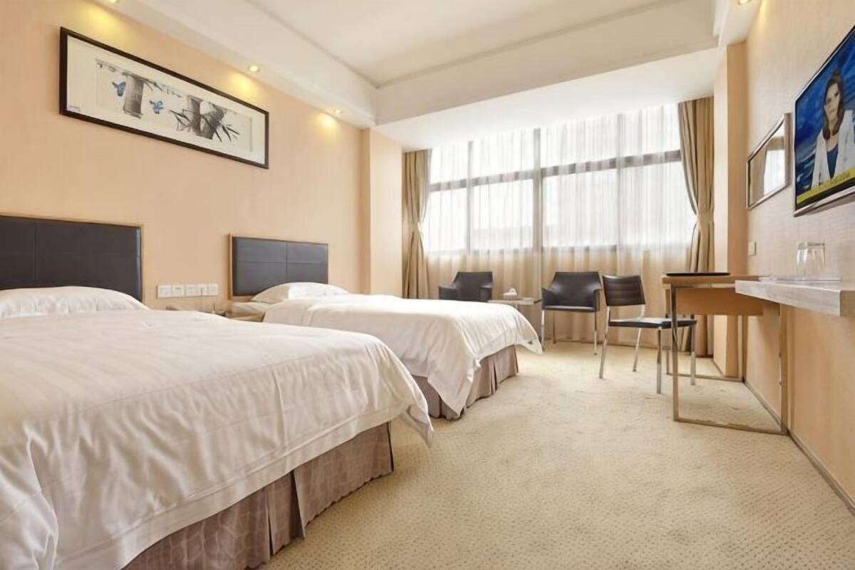 Habitación de hotel con dos camas, un escritorio, una silla y un ventanal grande.
