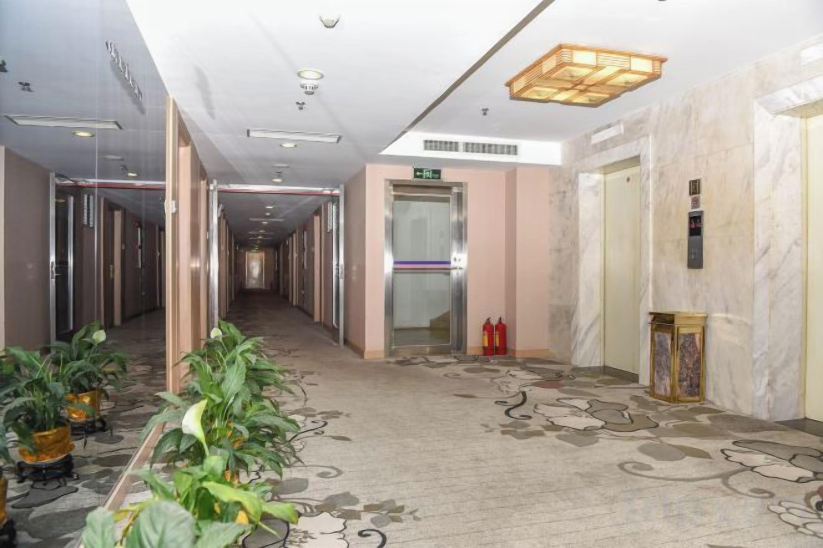 A hotel corridor with a marble floor, potted plants, and a fire extinguisher.