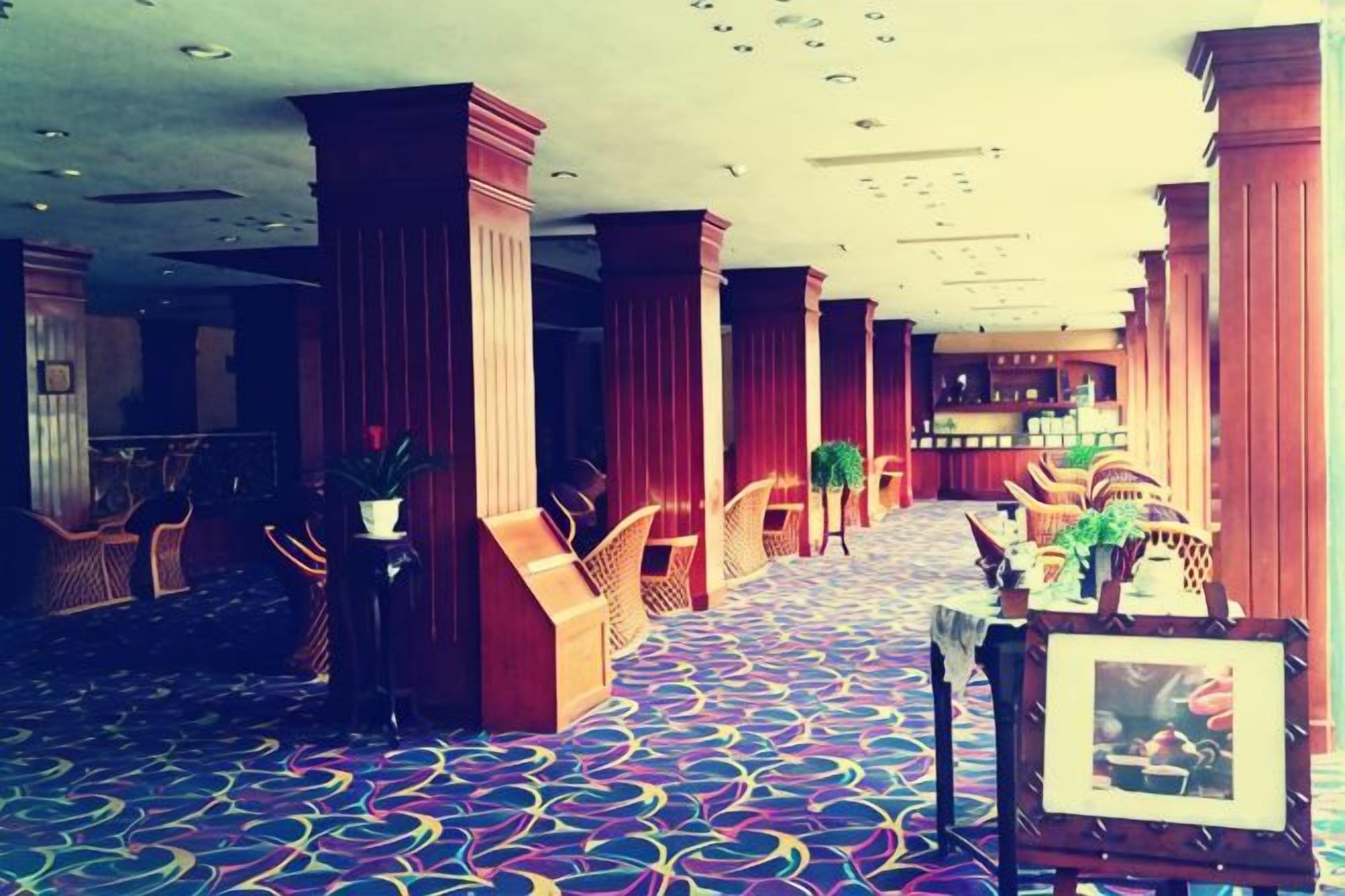 A hotel lobby with a patterned carpet, wooden columns, and seating areas.