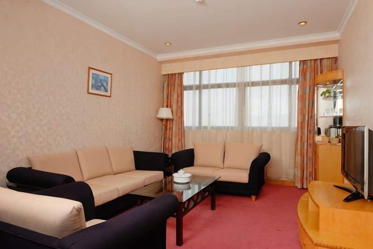 Habitación de hotel con sofá, mesa de centro, televisor y ventana con cortinas.