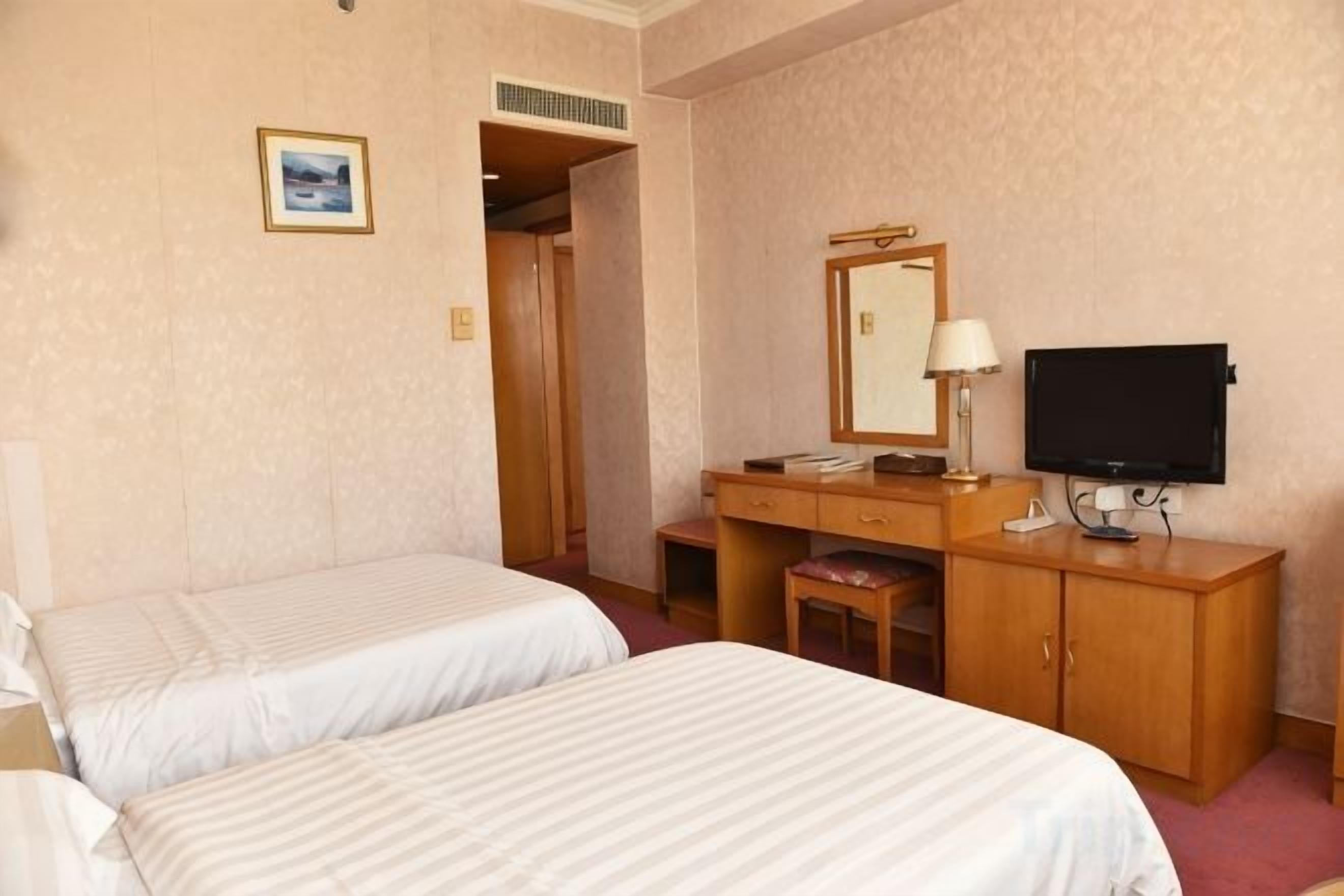 A hotel room with two beds, a desk with a mirror, a television, and a small stool.