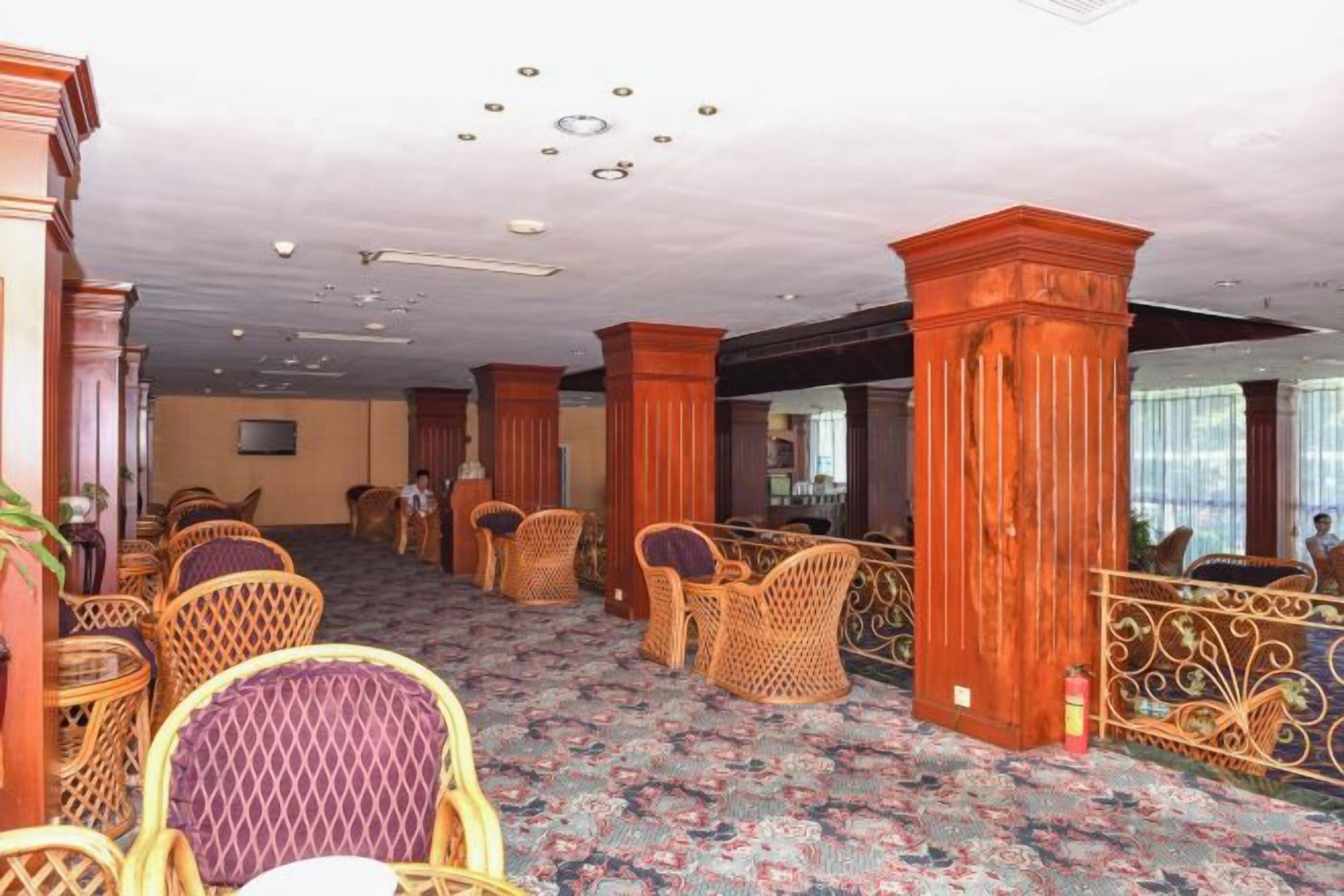 Un vestíbul d'hotel amb mobles de vimet, una catifes amb dibuixos i un gran pilar de fusta.